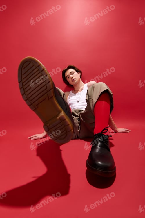 Preview: Stylish young man showcases trendy outfit against vibrant red backdrop