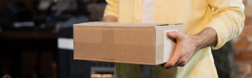 Preview: cropped view of publisher holding carton box in print center, banner