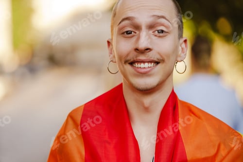 Preview: White man smiling and holding rainbow flag during pride parade at city