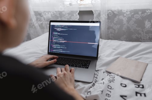 Preview: Young female programmer writes program code on a computer laptop in the bed at home. remote work