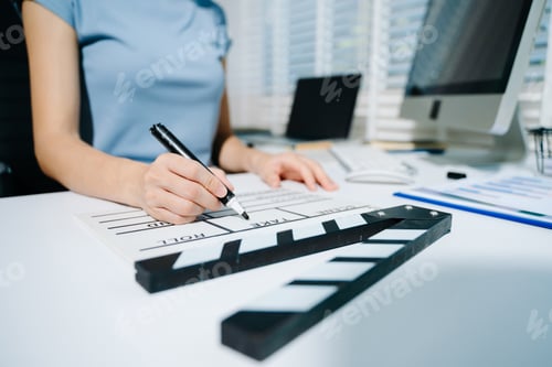 Preview: Creative female filmmaker working with tablet, clapperboard, and laptop in modern studio office.
