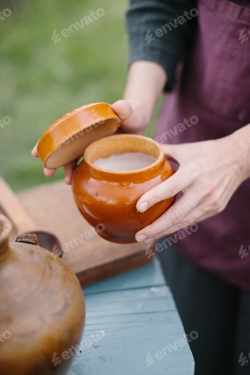 Preview: Hands Opening a Ceramic Pot Outdoors for Food Storage