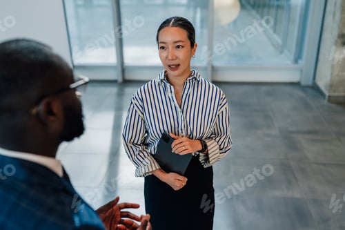 Preview: Businesswoman holding tablet talking to businessman in office hallway