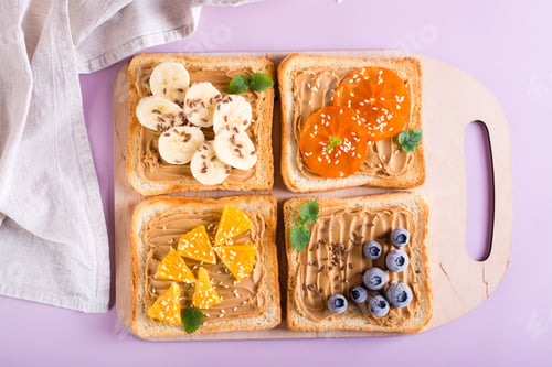 Preview: Toast with peanut butter, fruits, berries, flax seeds and sesame seeds on a cutting board. Top view.
