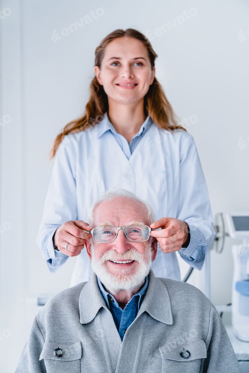 Preview: Vertical photo of a female young oculist fitting glasses to elderly male patient