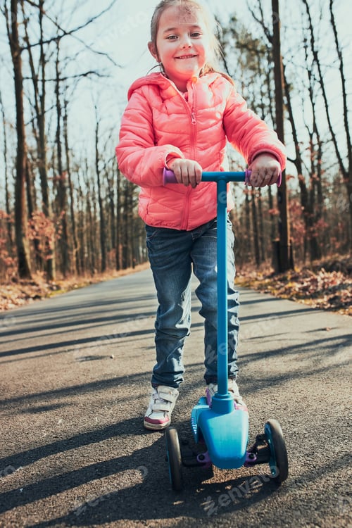 Preview: Little girl playing in the park, riding a scooter, having fun on sunny autumn day