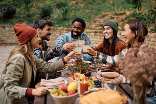Preview: Happy friends toasting while eating at picnic table on a patio.