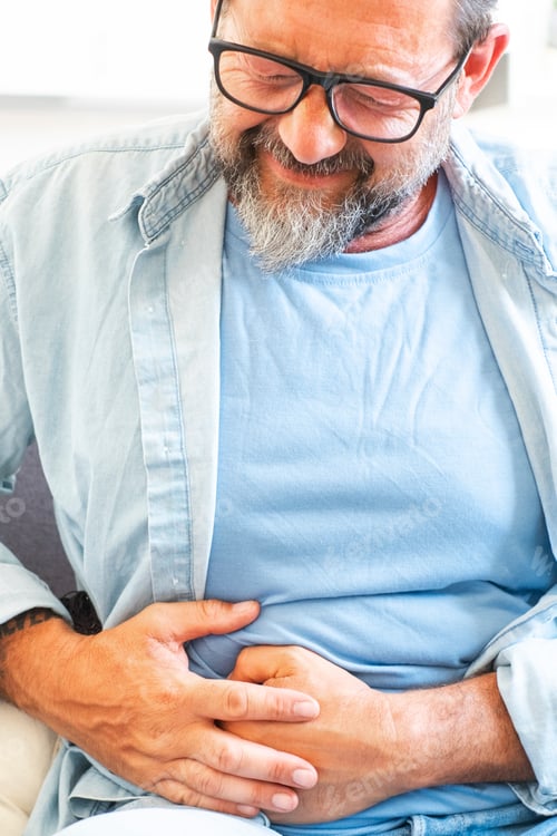 Preview: Unhappy mature man, sits on comfortable sofa in cozy living room, holds his hands on his stomach,