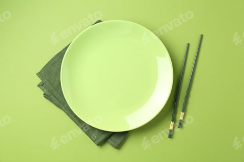 Preview: Stylish plate, chopsticks and napkin on green background, flat lay