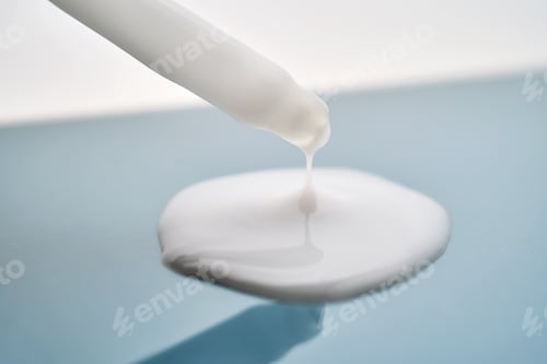 Preview: Pipette with white cream serum on blue background.