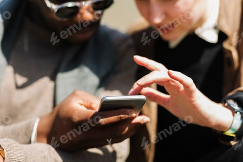 Preview: Two individuals are focused on a smartphone screen that one of them is holding.