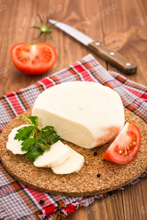Preview: Sliced Adyghe cheese, tomato and parsley on a substrate on a wooden table