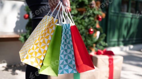 Preview: Close-up women’s hand carrying colourful shopping bags over Christmas tree background