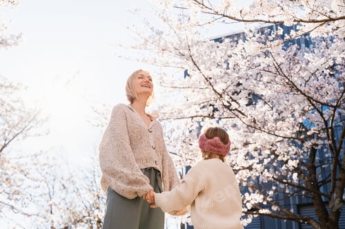 Preview: Mother and daughter are happy together in blooming trees garden in front of house. Mother's day