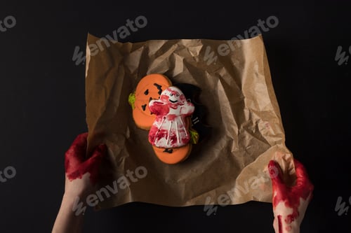Preview: partial view of hands wrapping halloween cookies in baking paper