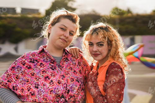 Preview: Young women smiling on camera during LGBT pride parade with sunset in the background