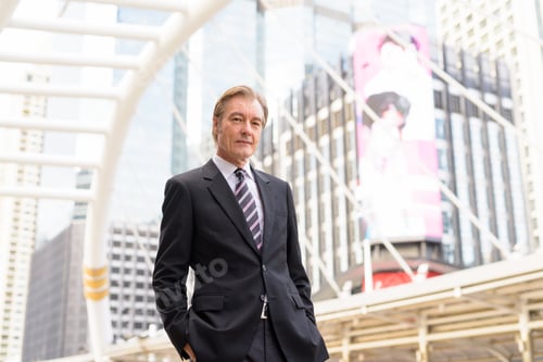 Preview: Mature handsome businessman wearing suit at skywalk bridge in the city
