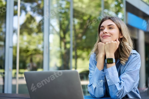 Preview: Dreamy woman sitting with laptop outdoors on street. Smiling businesswoman daydreaming, imaging