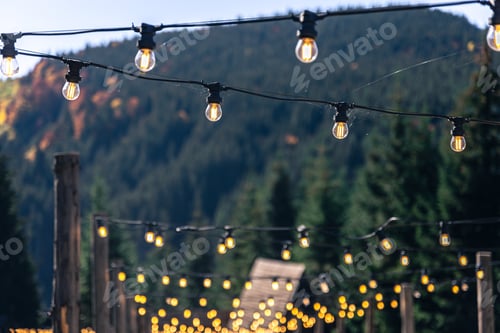Preview: Decorative light bulbs on wooden poles in a mountainous area.