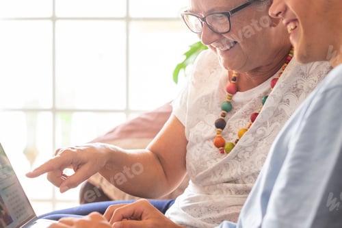 Preview: Cheerful grandmother and teenage grandson sitting together on the couch at home using laptop