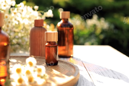 Preview: Bottles of essential oil and flowers on white wooden table outdoors, space for text