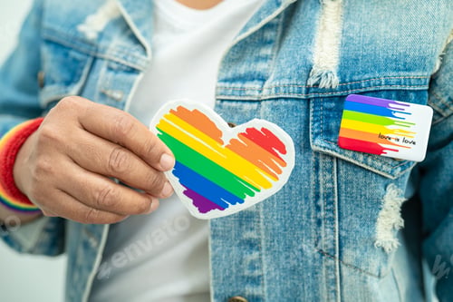 Preview: Asian lady wearing rainbow flag wristbands and hold red heart, symbol of LGBT pride month celebrate