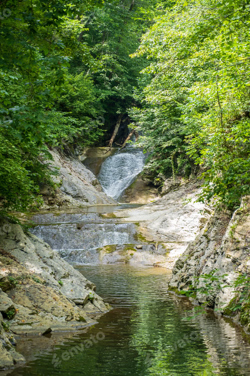 Preview: Waterfall covered by green lush trees and stony formations