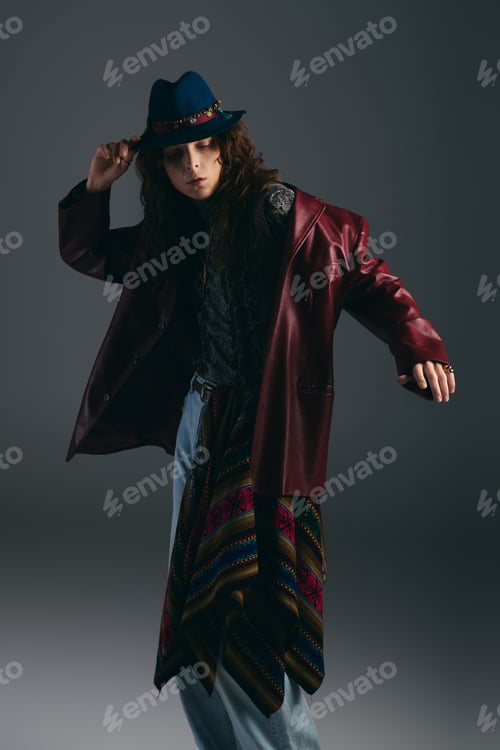 Preview: Stylish young man poses in a fashionable outfit with a hat in a modern studio setting