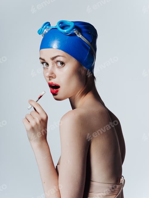 Preview: Woman swimmer in a blue swimming cap is smoking on a light background
