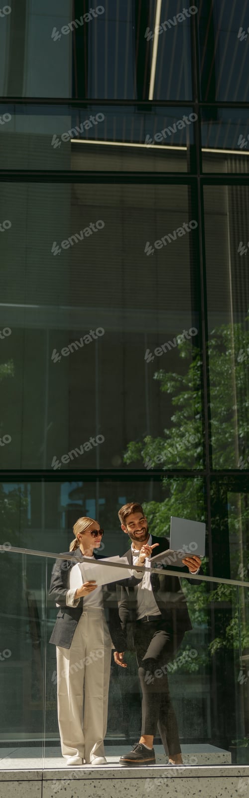 Preview: Business colleagues working with documents while standing on background of modern office building