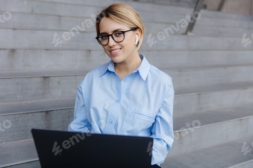 Preview: Smiling blonde sitting outdoors with laptop