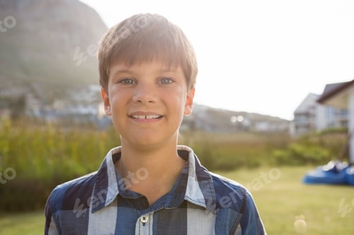 Preview: Preteen boy standing in grassy suburban field wearing blue and white plaid shirt under bright sun