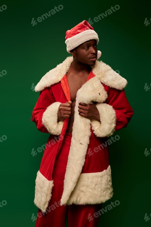 Preview: handsome african american man in santa claus costume standing and looking away on green backdrop