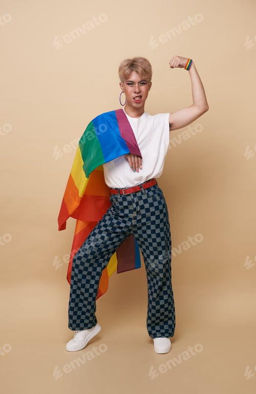 Preview: Youth asian transgender LGBT with Rainbow flag on shoulder isolated over nude color background.