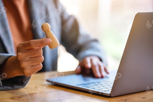 Preview: Businesswoman leader holding and choosing wooden people while working on laptop computer in office