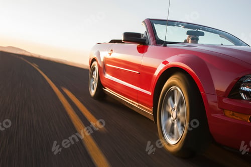 Preview: A low angle view of a convertible sports car moving on a highway late in the day.