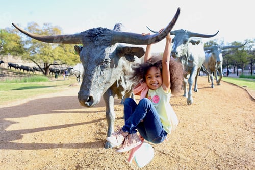 Preview: Happy young girl sitting under a bull statue