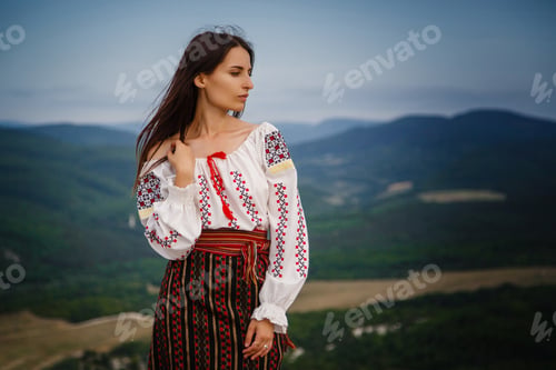 Preview: Attractive woman in traditional romanian costume on mountain green blurred background.