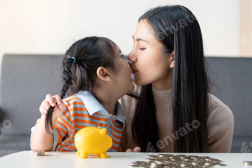 Preview: Mother Kissing Daughter While Teaching Money Saving Habits with Piggy Bank