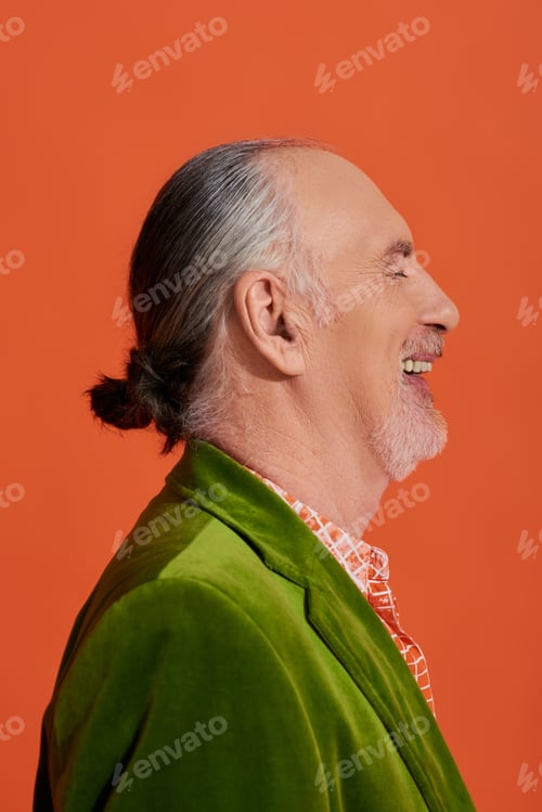 Preview: side view of excited and fashionable older model laughing with closed eyes on vibrant orange