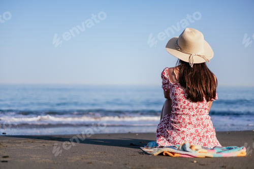 Preview: carefree young woman wearing summer hat relaxing happily sitting on sand at beach