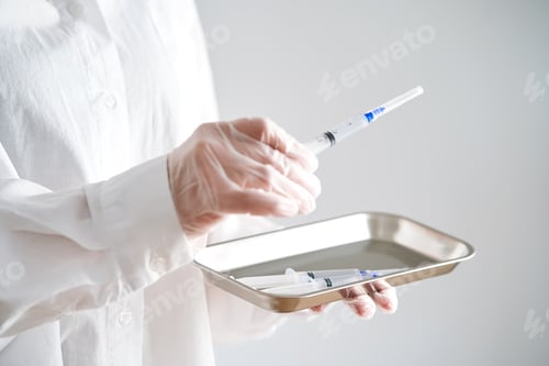 Preview: Anonymized photo of a doctor's hands holding a tray and a syringe with a needle.