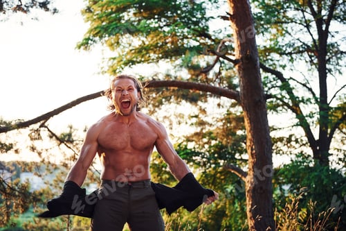 Preview: Looks behind. Handsome shirtless man with muscular body type is in the forest at daytime