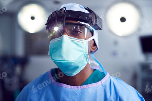Preview: Portrait Of Male Surgeon Wearing Protective Glasses And Head Light In Hospital Operating Theater