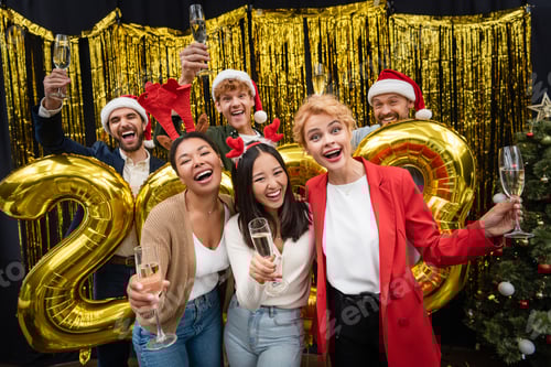 Visualização: Empresárias inter-raciais segurando champanhe perto de empresários e balões em forma de números de 2023