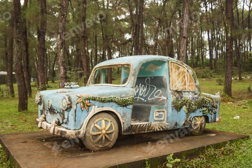 Preview: A blue retro car in the middle of a pine forest. The car is covered in graffiti.