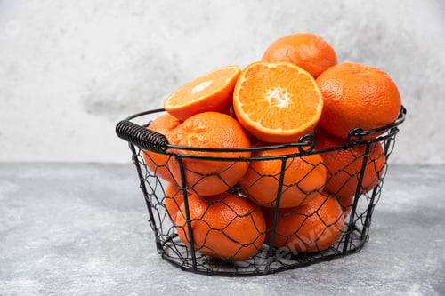 Preview: A metallic black basket full of juicy orange fruit on stone background