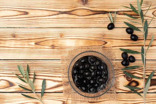 Preview: Olives in a bowl on wooden background, top view