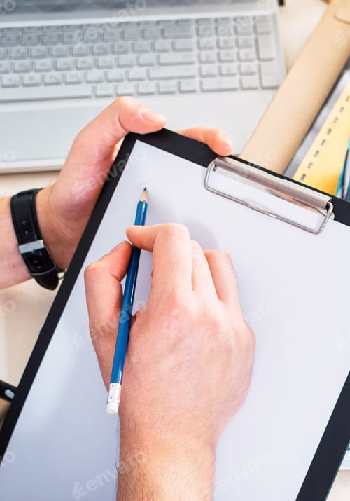 Preview: Closeup of male hands writing a report on a clipboard on background of the desk