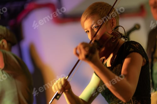 Preview: A female violinist plays the violin. Band performs on stage, rock music concert.